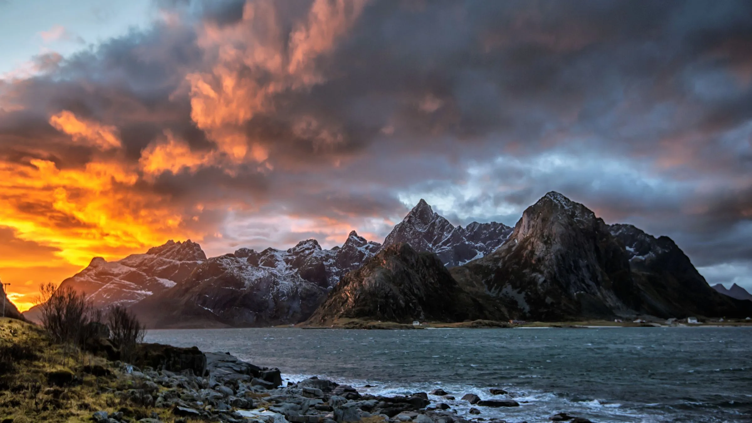 Orange winter light breaking behind a dark mountain chain above the sea.