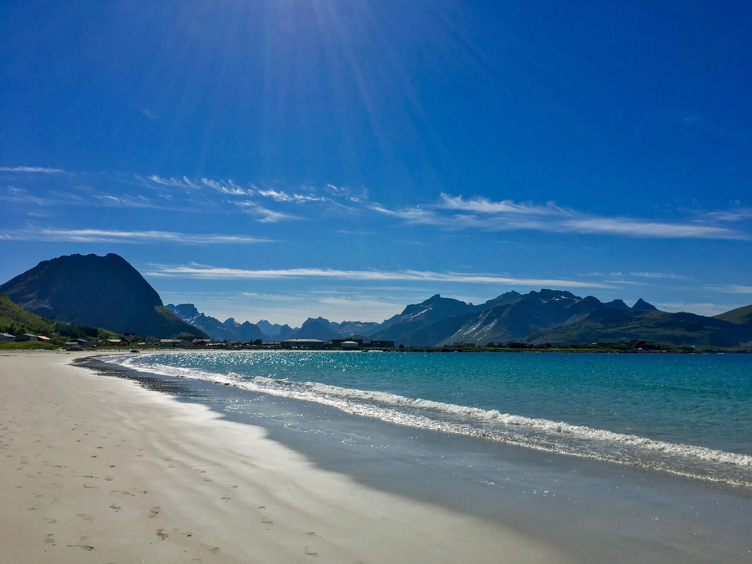 A white sand beach curves toward dark mountains beneath a clear blue sky.